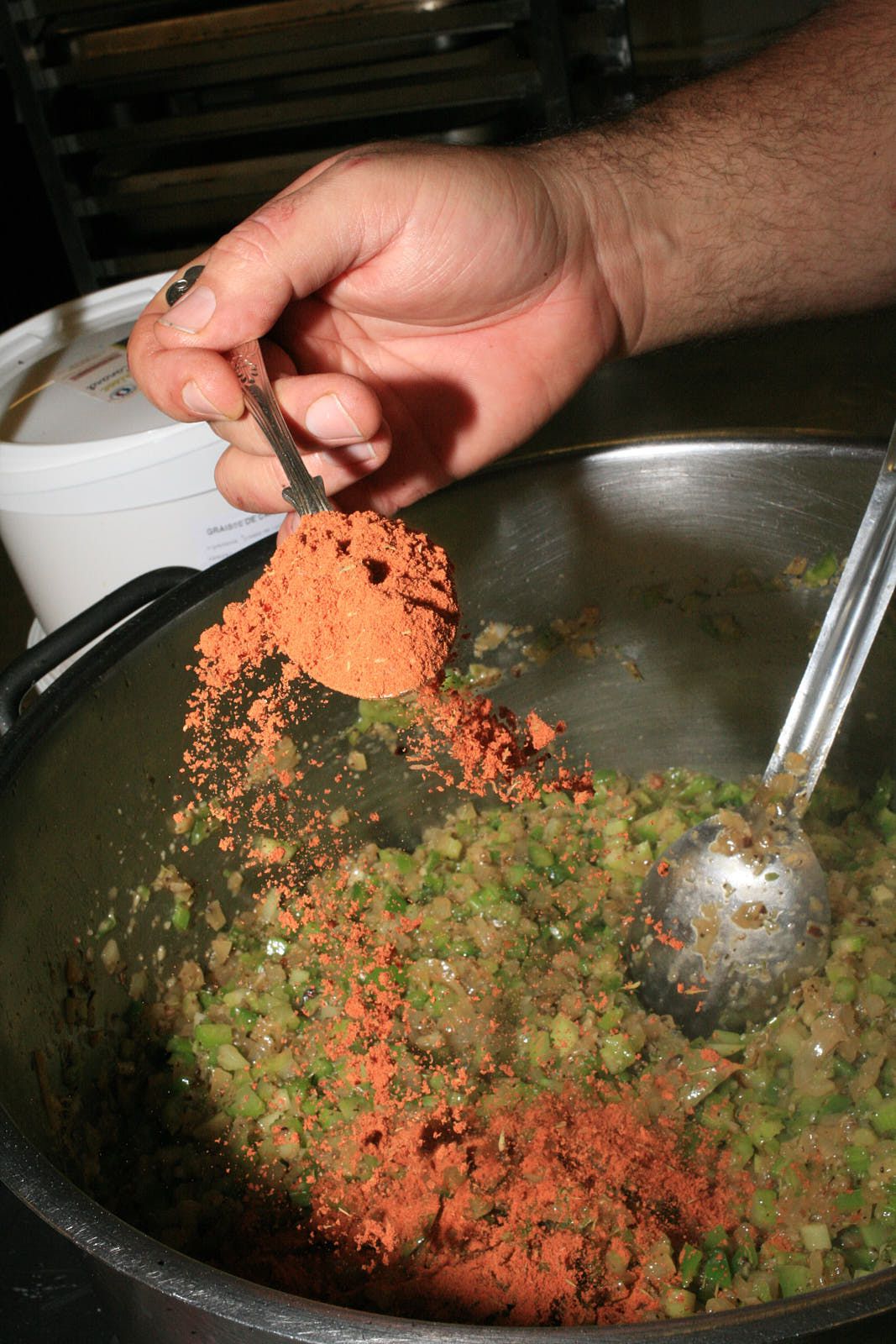 A close-up of a heaped teaspoon of cayenne and paprika being spooned into the gumbo base