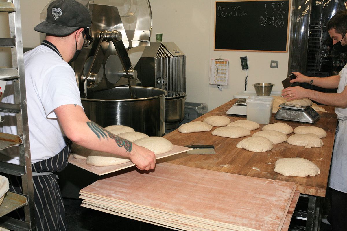 A baker places loaves on to a wooden bench ready for shaping
