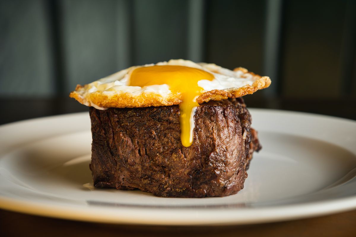 A white plate with a filet of steak topped with a runny fried egg.