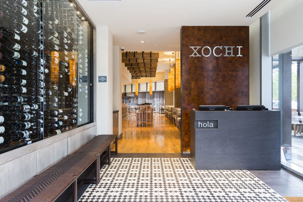 A lobby entrance at a restaurant with a sign that says Xochi hanging above a front desk.