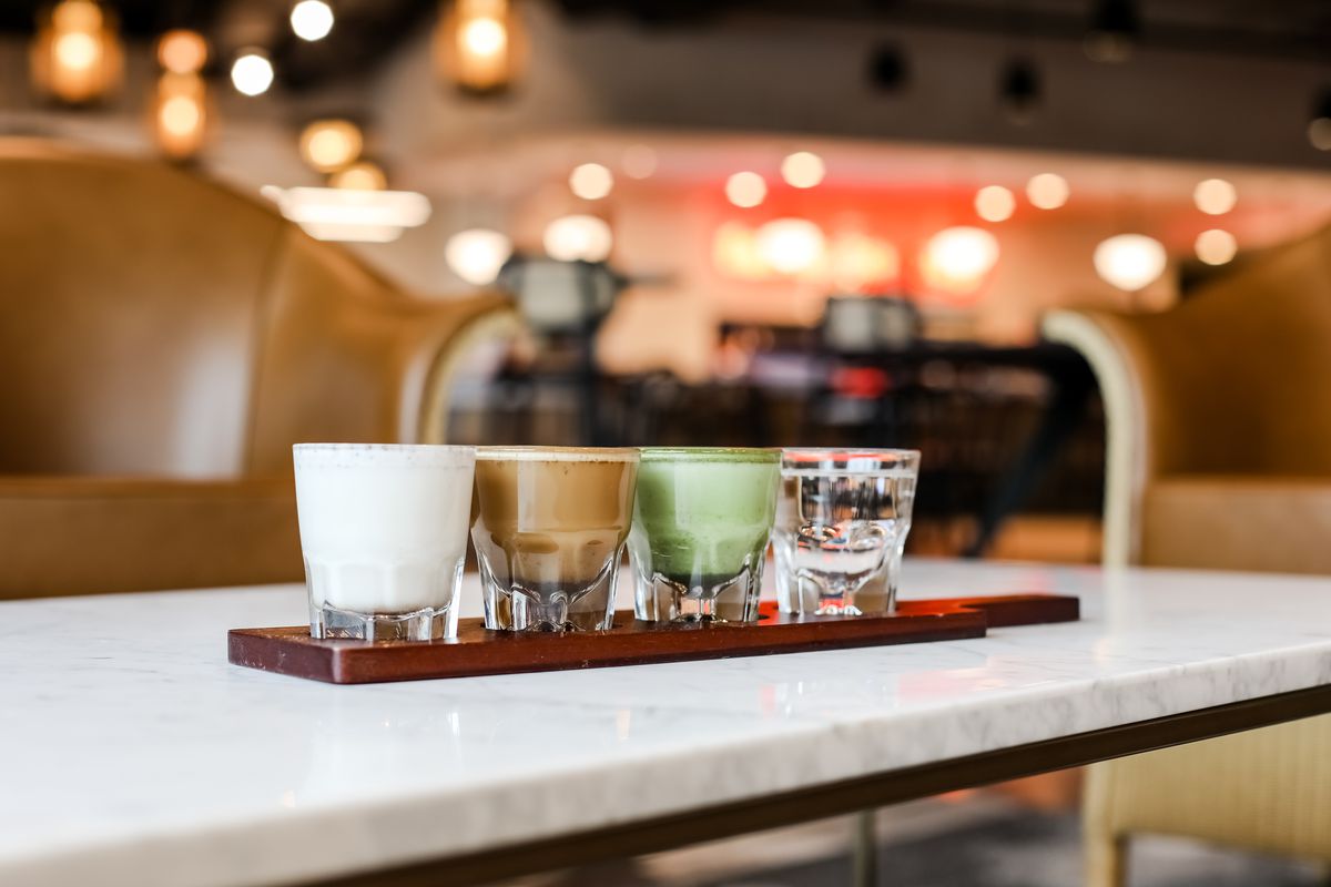 A flight of cortado shots are lined up on a marble bartop.