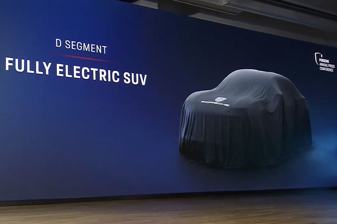 PowerPoint slide on Porsche press conference stage with a big SUV covered by a black cloth. The slide reads, “D segment fully electric SUV.”