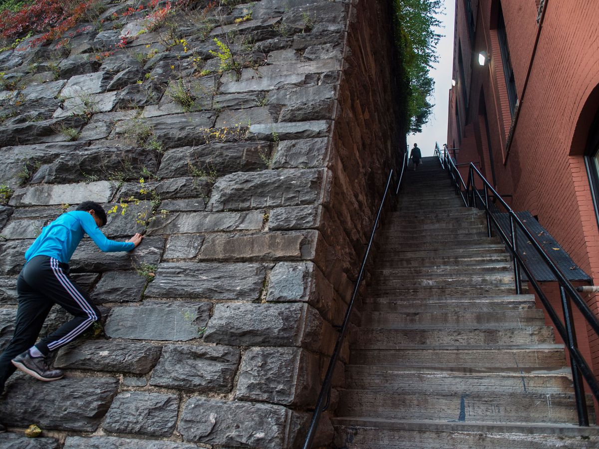 A set of steep stairs between a brick building and a brick wall. A child climbs the left wall.