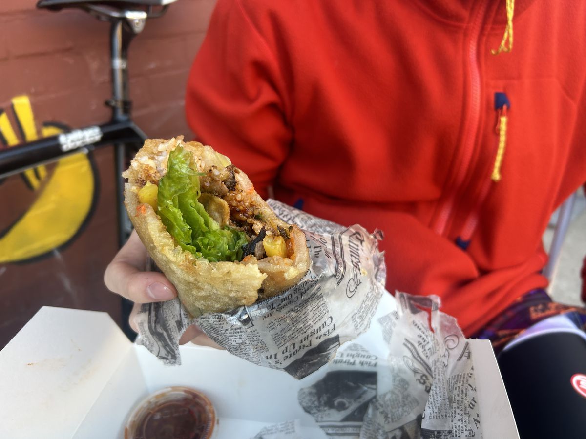 A person wearing a red sweater clutches a burrito overflowing with bulgogi.