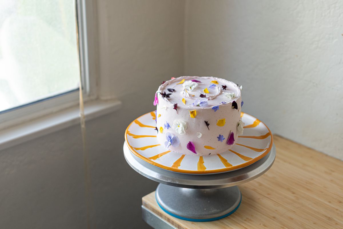 Iced cake on a striped plate with multicolored flower petals around the top and sides.
