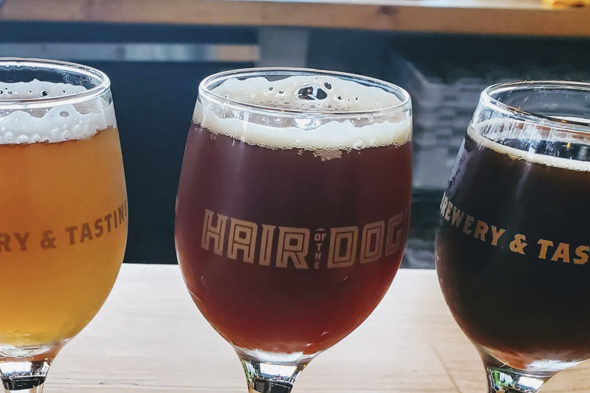 Amber hued, hazelnut colored, and coffee brown beers sit on a table in Hair of the Dog branded glassware.