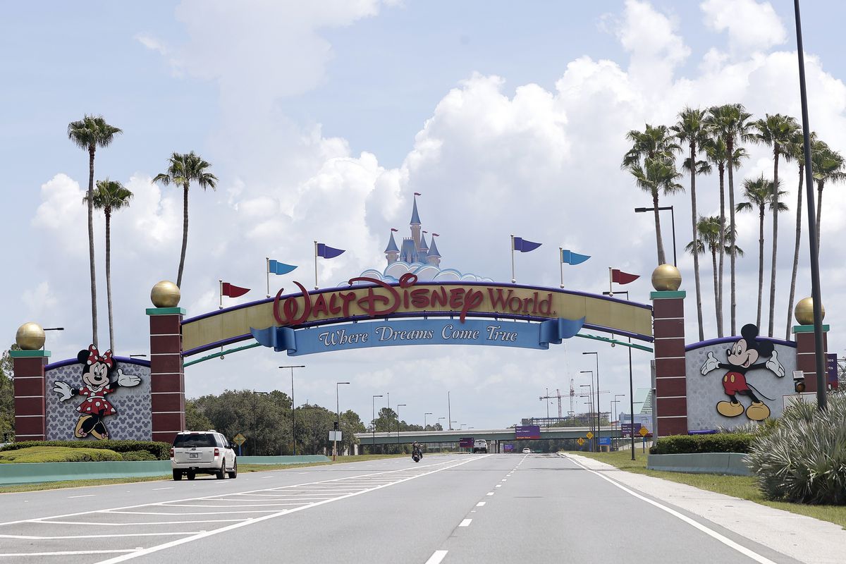Cars drive under a sign greeting visitors near the entrance to Walt Disney World, in Lake Buena Vista, Fla.