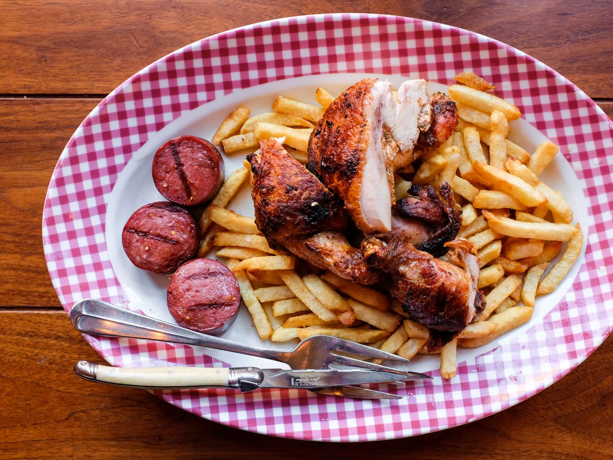 A plate with grilled chicken and slices of summer sausage, and french fries