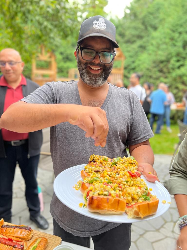 A man sprinkles something onto a plate of chaat dogs.