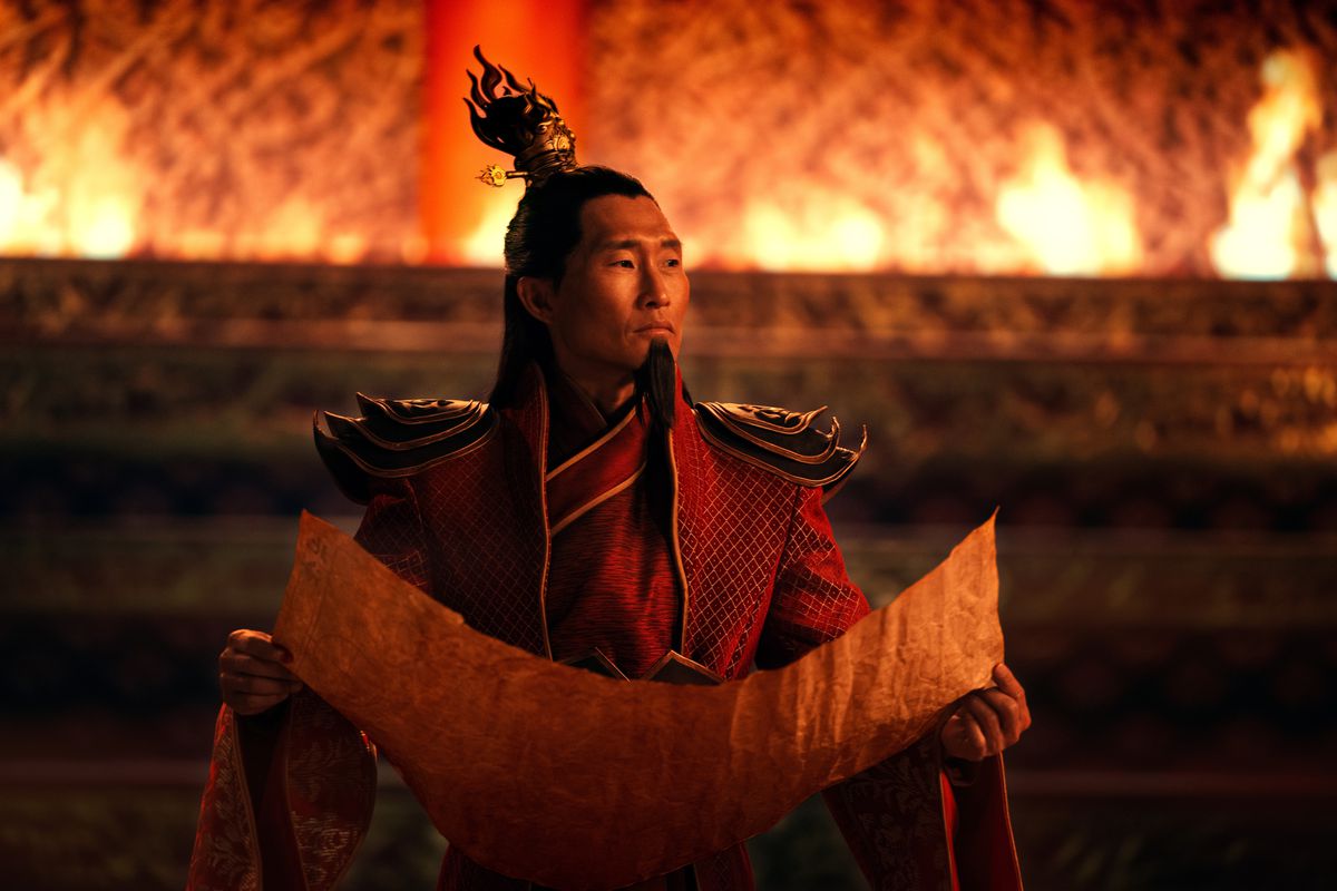 Daniel Dae Kim as Fire Lord Ozai holds an open scroll in a stone room lit by open flames in Avatar: the Last Airbender
