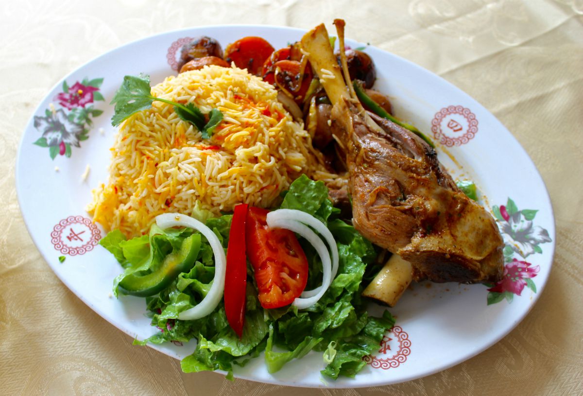 An oval plate piled high with salad, rice, and a bone-in lamb shank.