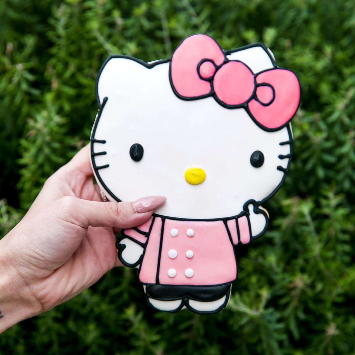 A hand holds a giant frosted cookie decorated like Hello Kitty.