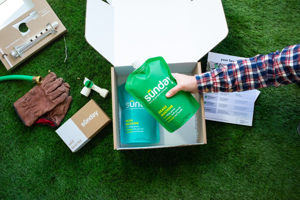 A hand grabs a green fertilizer pouch from a cardboard box. 