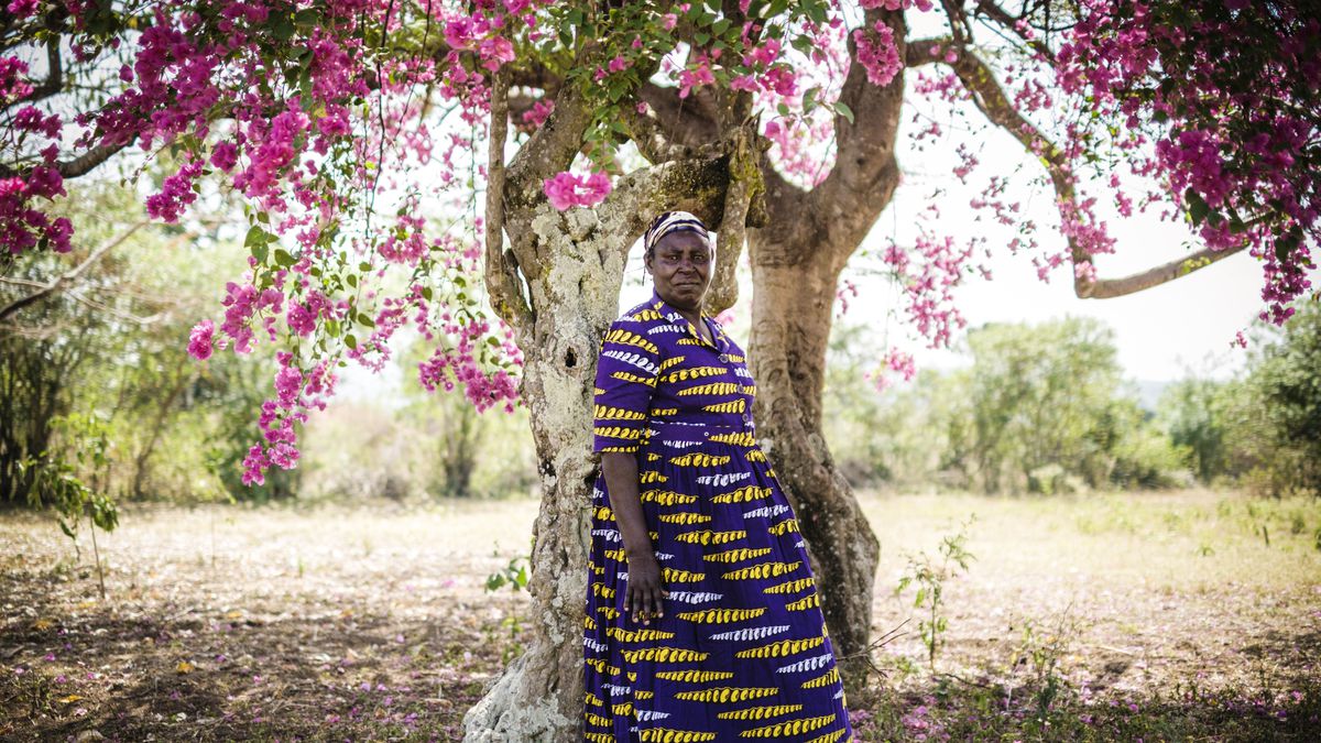 A Kenyan woman standing outside under a flowering tree.