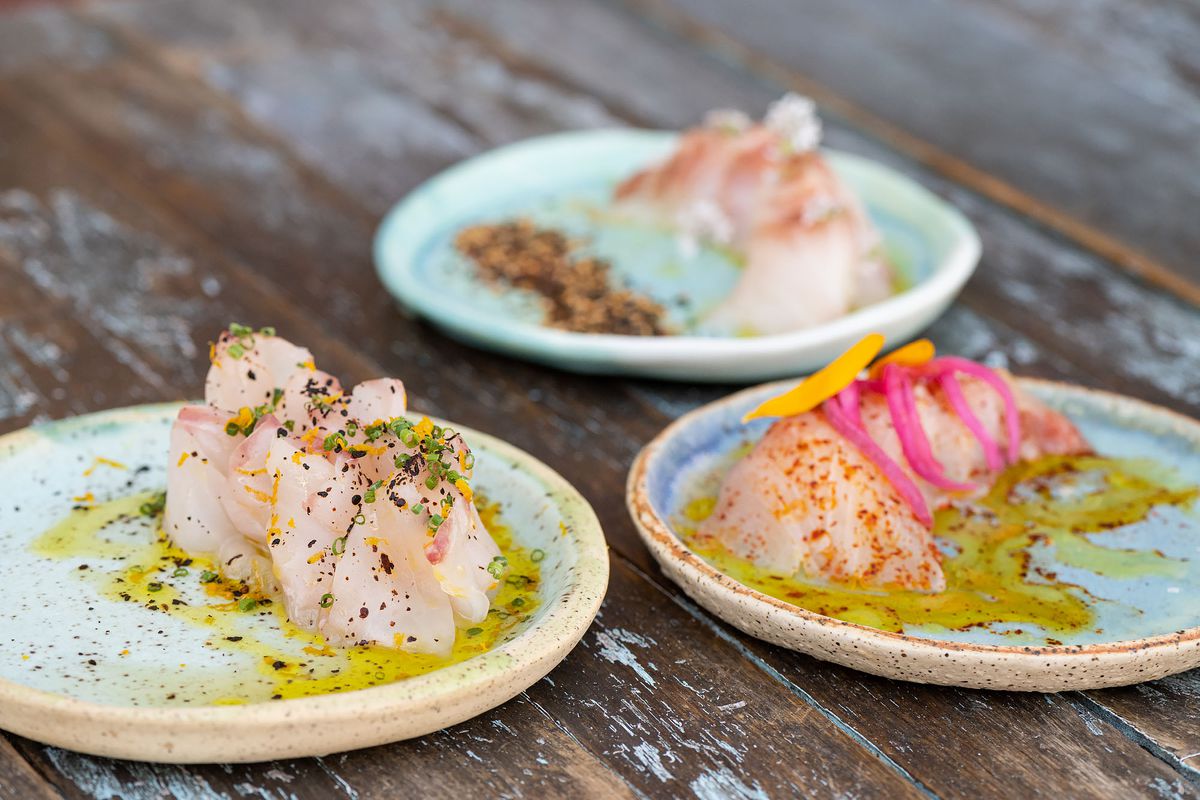 Three plates with slices of raw fish on them, covered in olive oil and pickled onions.