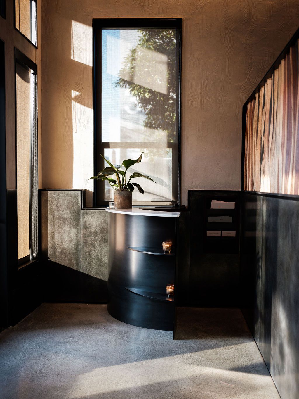 The entry of Flour + Water with a rounded black metal host stand and concrete floors.