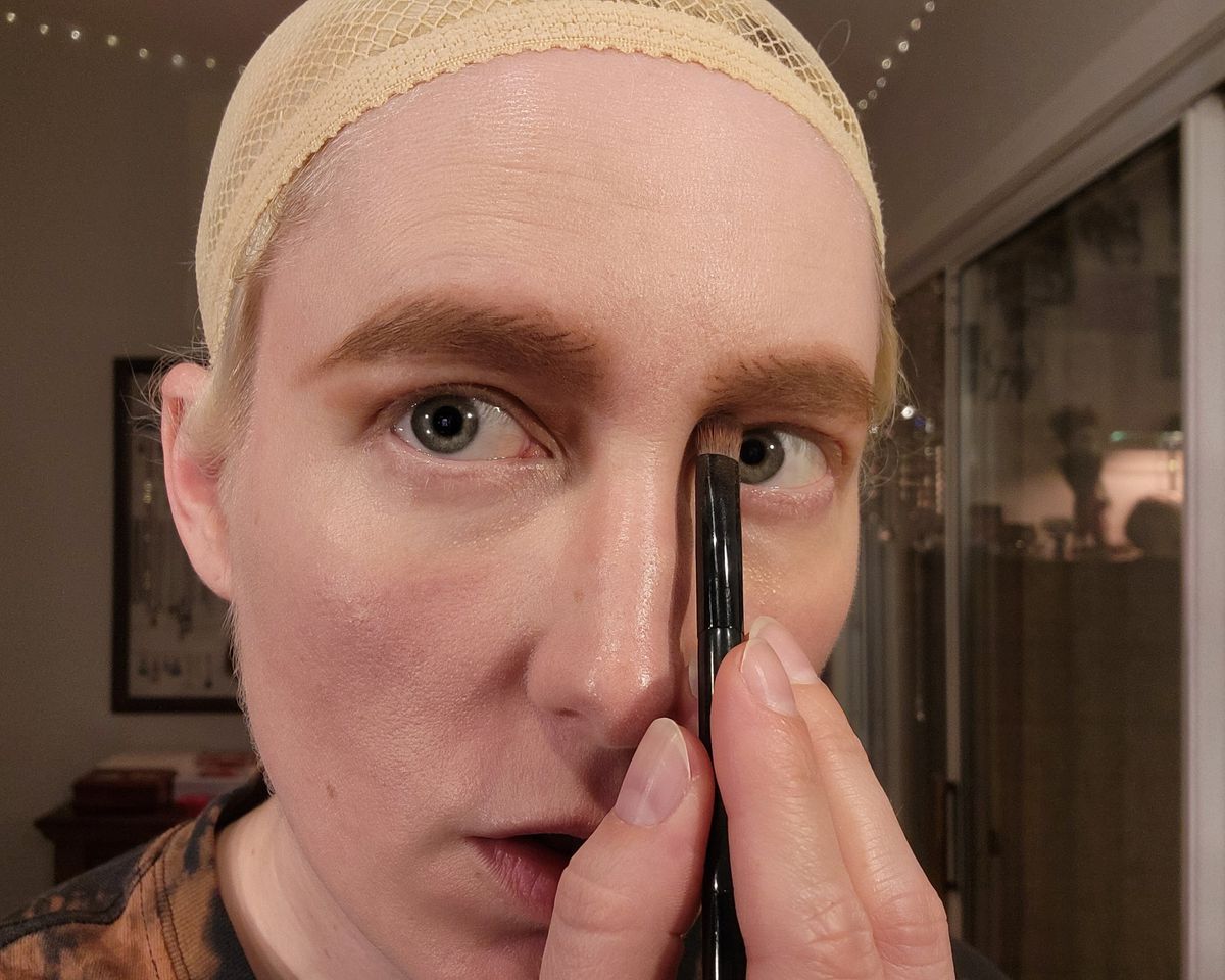The author uses a brush to apply eyeshadow under her brows