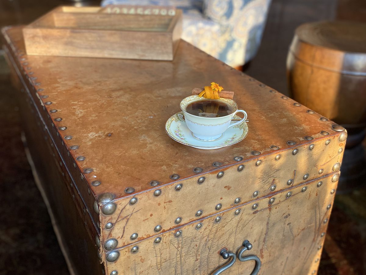 A white tea cup filled with apple cider sitting on a brown trunk. 