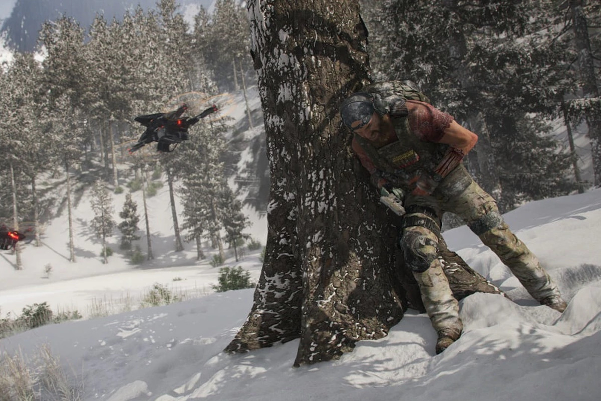 A soldier leans behind a tree on a snowy mountain to avoid detection by a hovering drone