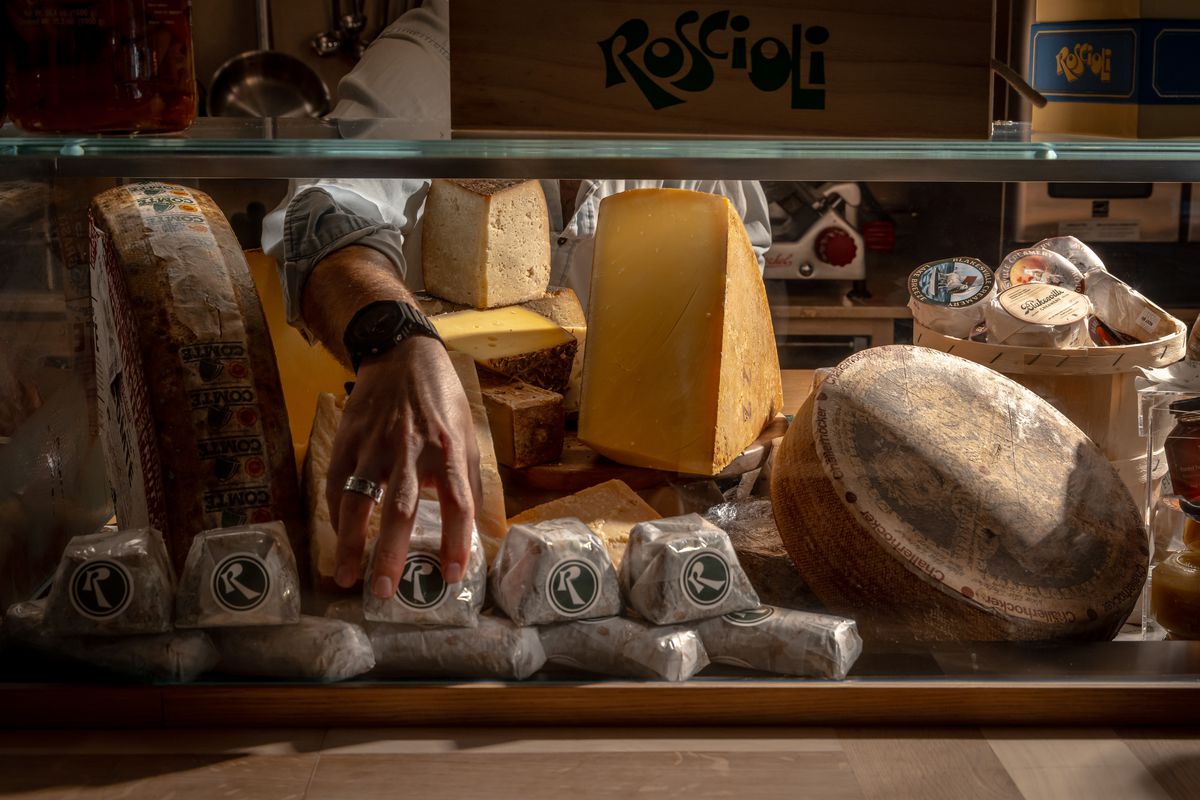 A hand grabs cheeses from Roscioli’s cheese case.