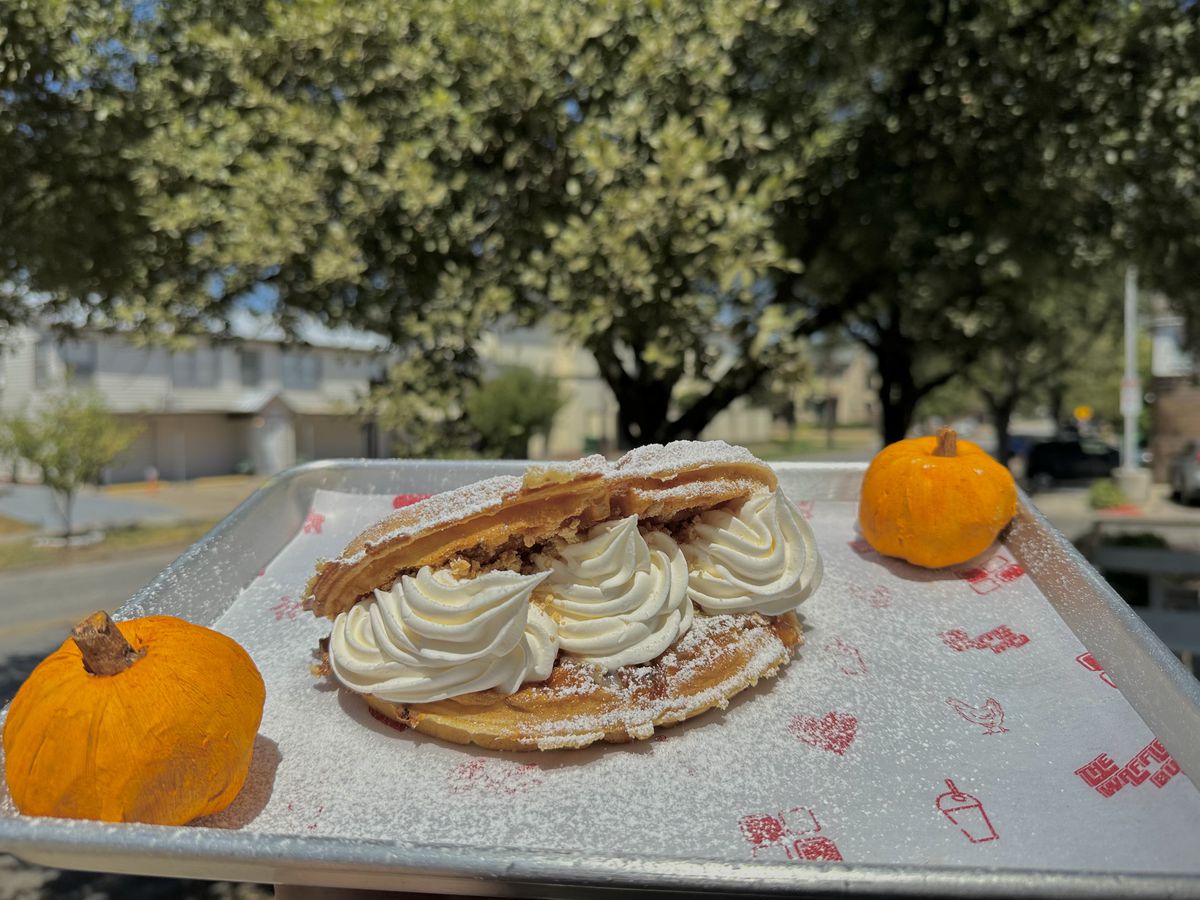 A pumpkin pie waffle filled with pumpkin pie sauce, sweet cream, and whipped cream, on a tray with two miniature pumpkins.