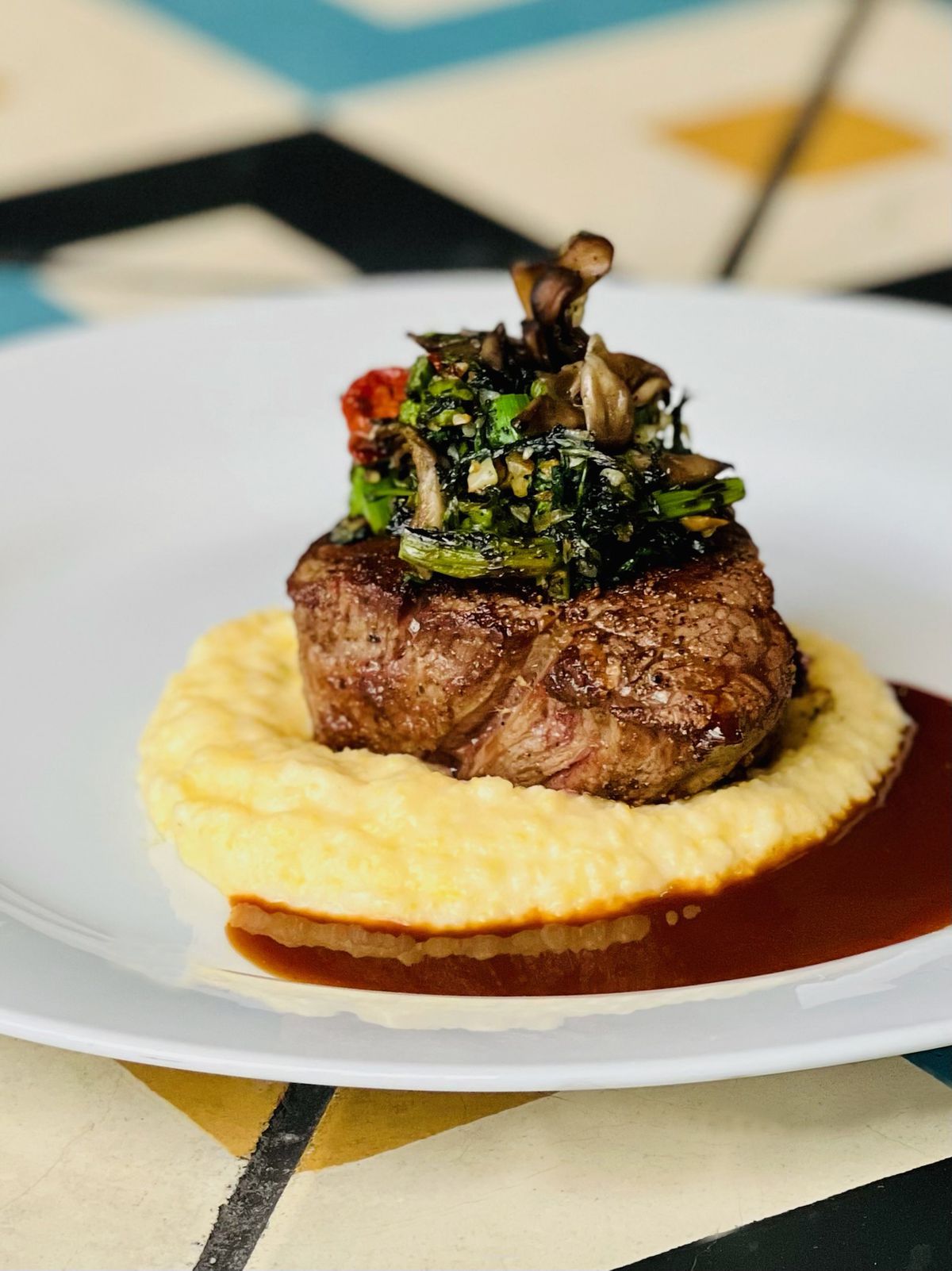 A tall shot of a seared steak over yellow polenta on a white plate.