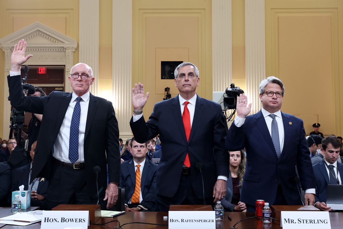 Three white men with white hair, all wearing dark suits, white shirts and ties, stand while raising their right hands behind a large brown table.