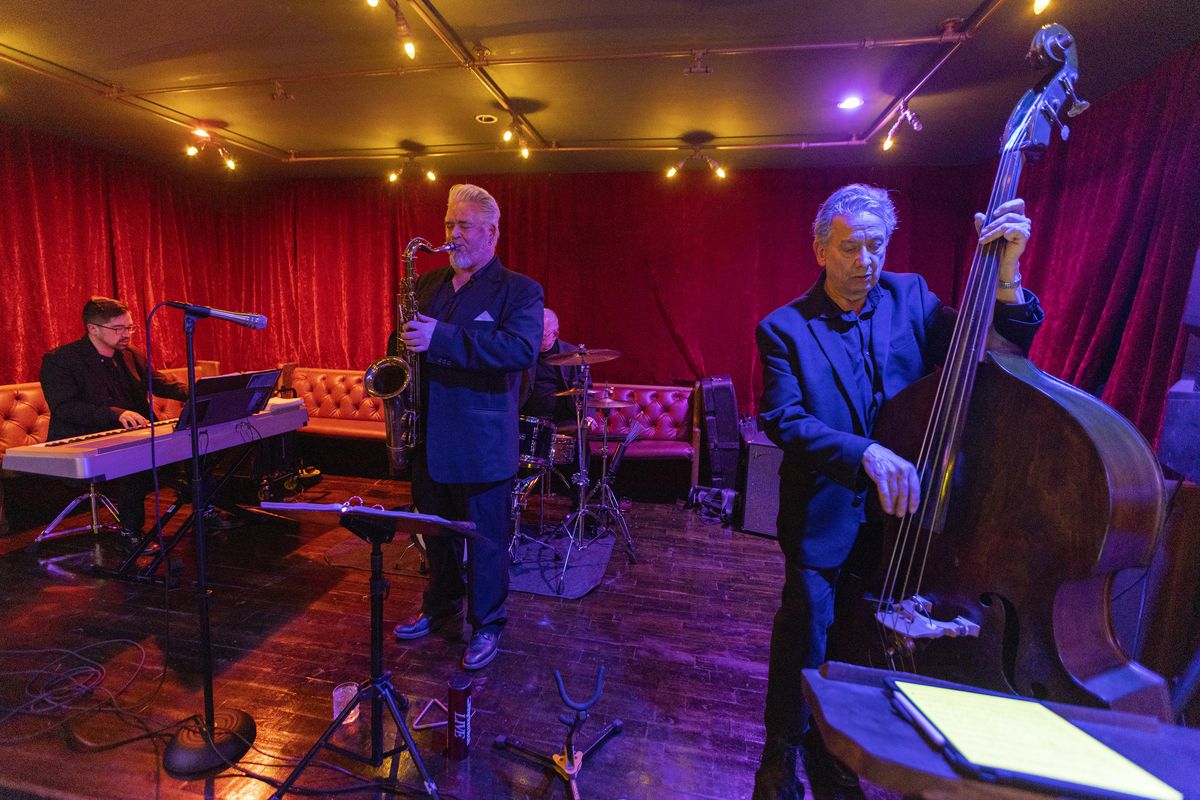 A group of jazz musicians play on a stage inside a speakeasy-style bar.