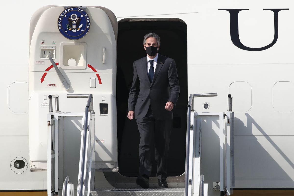 Secretary of State Antony Blinken stepping out of a plane’s cabin door onto the jetway stairs.