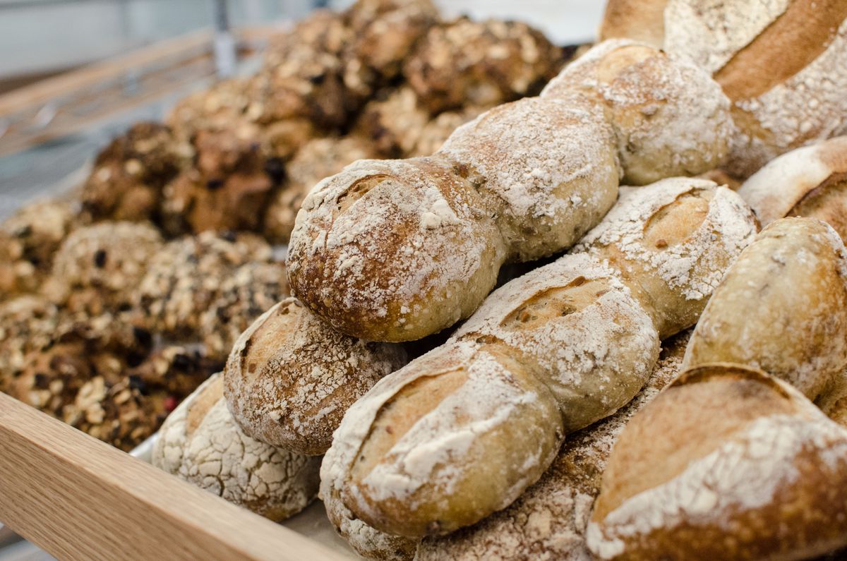 Loaves of bread and muesli rolls are piled onto a wooden display shelf.