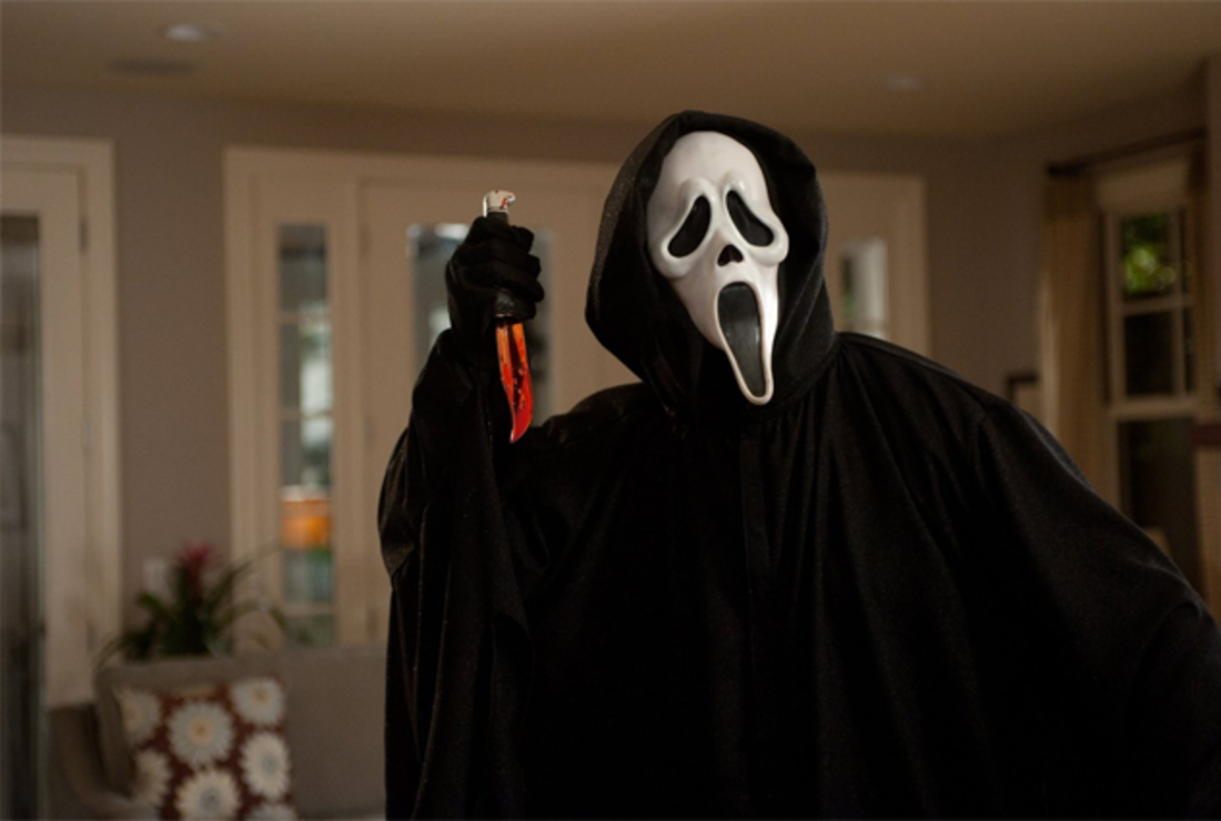 A serial killer in a ghoulish mask and black cloak touts a blood-covered knife.