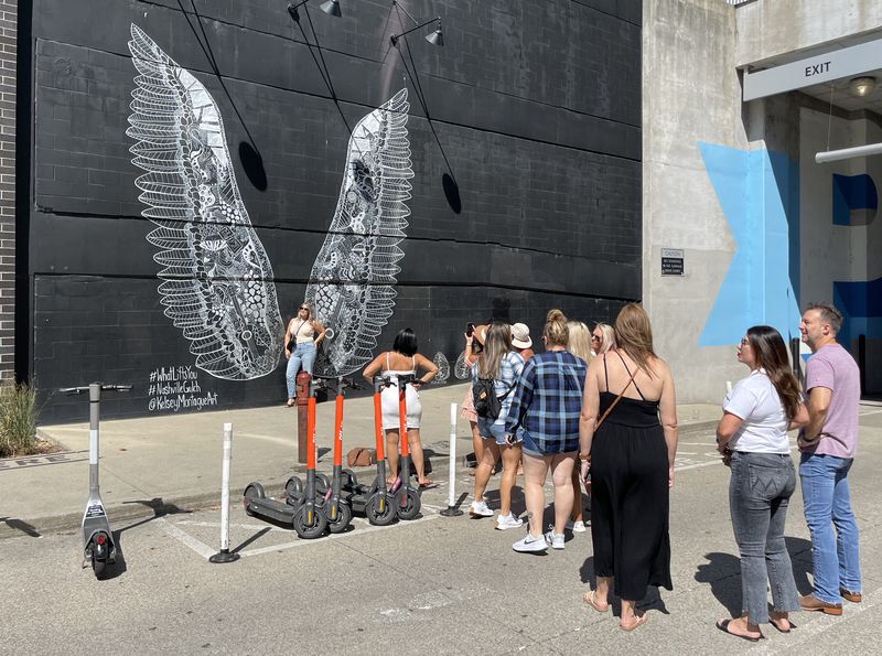 A line of people waiting to take photos in front of a large mural of wings. 