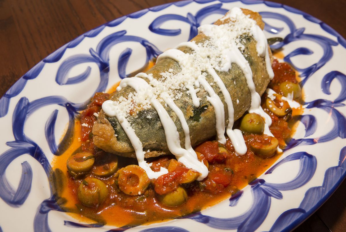 A fried, stuffed poblano pepper in a red sauce with crema and cheese on top.