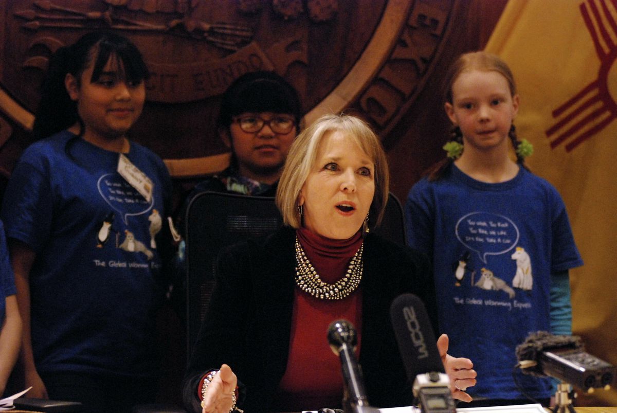 New Mexico Gov. Michelle Lujan Grisham, center, signs an executive order for state agencies to aggressive pursue strategies to reduce greenhouse gas emissions on Tuesday, Jan. 29, 2019, in Santa Fe, N.M. flanked by student activists on global warming issu