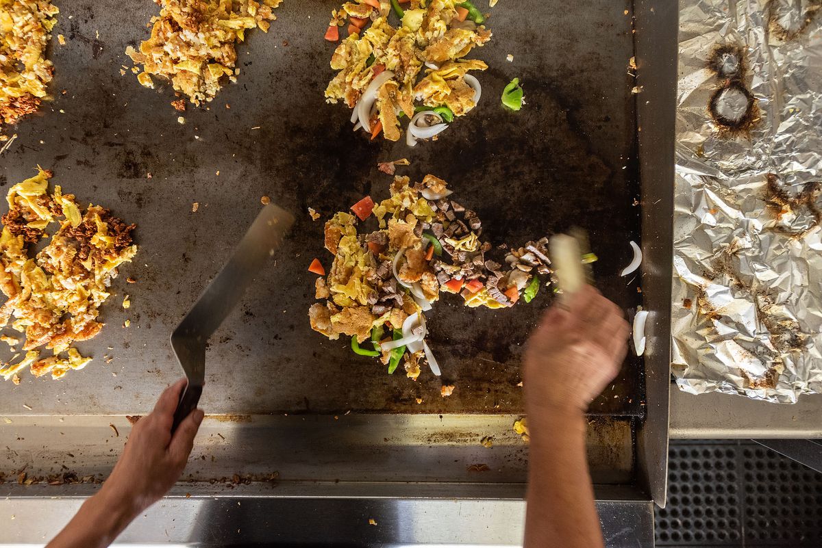 Shown from above, a worker deals with eggs on a large griddle.