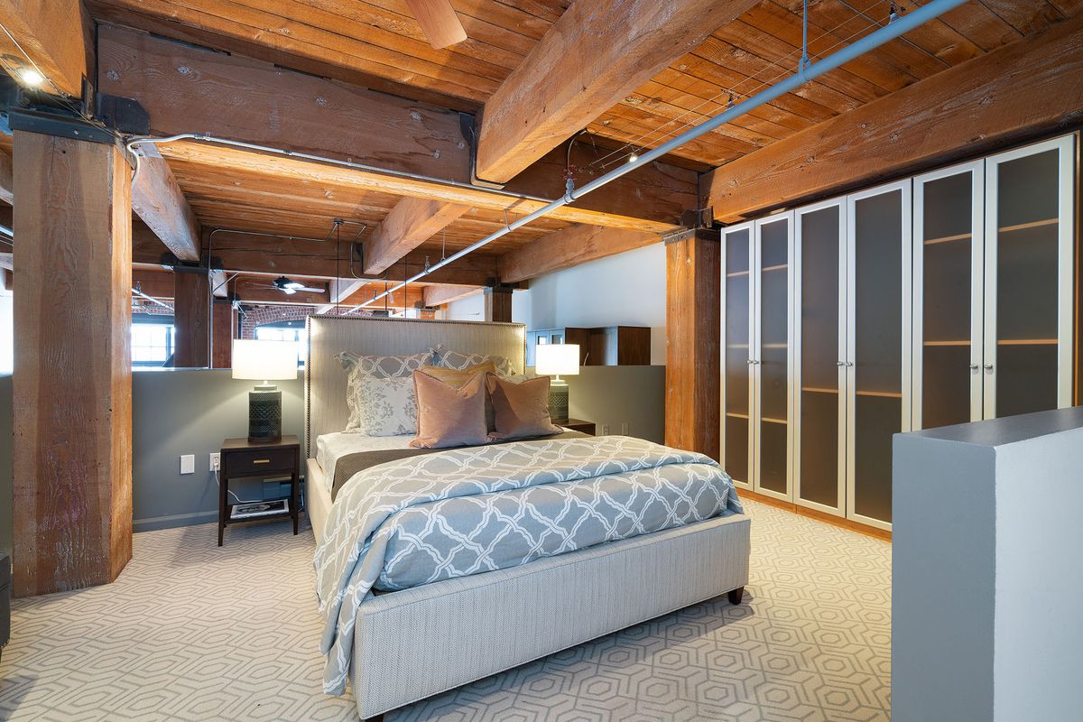 A gray patterned bed sits in the center of a lofted bedroom with built-in cabinets for a closet. 