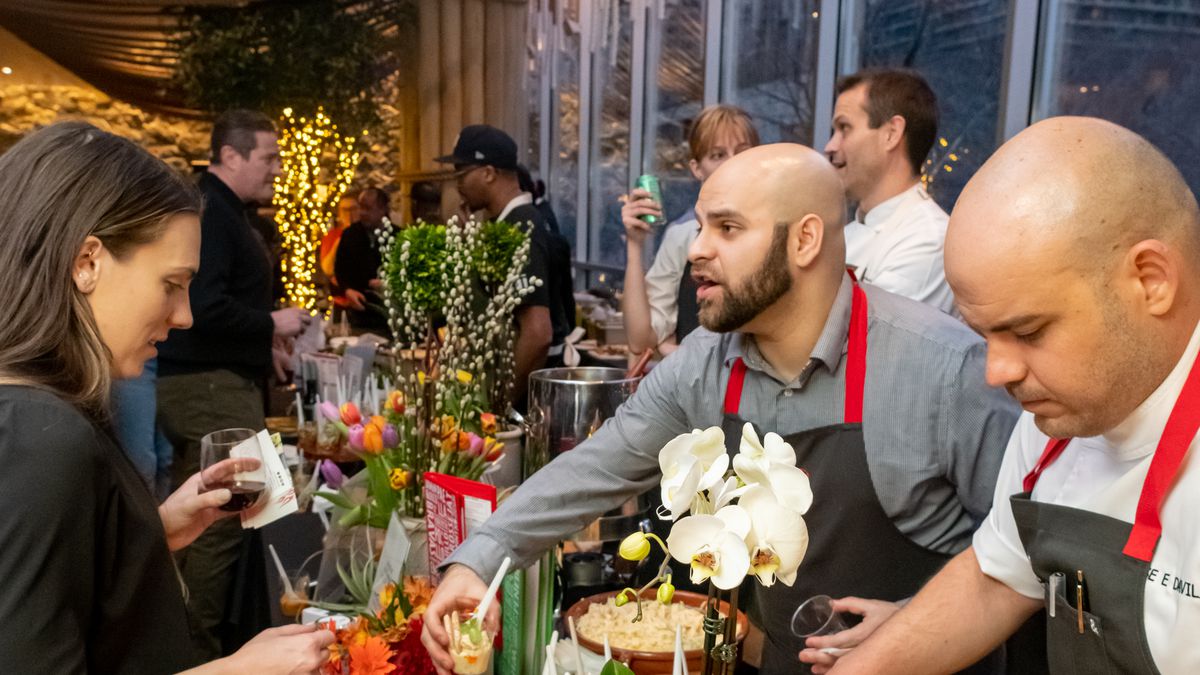 Chefs talk and interact with people across a table at a fundraiser.
