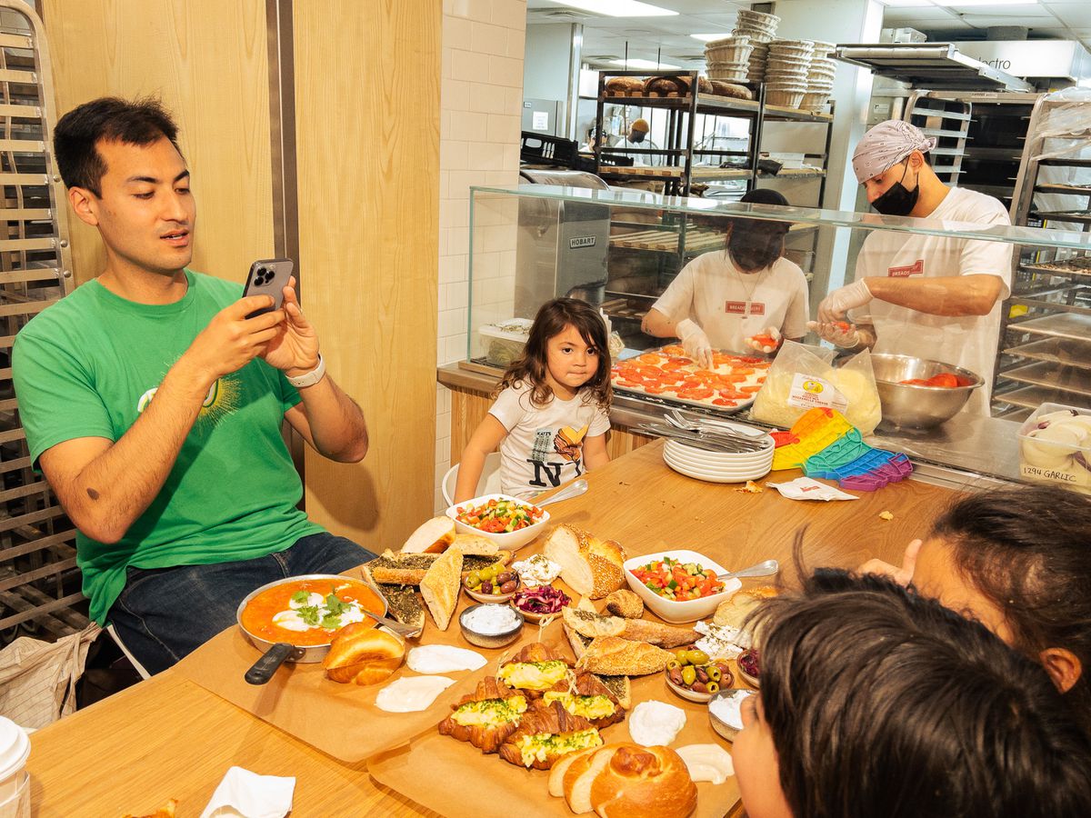 A man, Mike Chau, takes a photo of his children and a colorful spread of food using an iPhone.