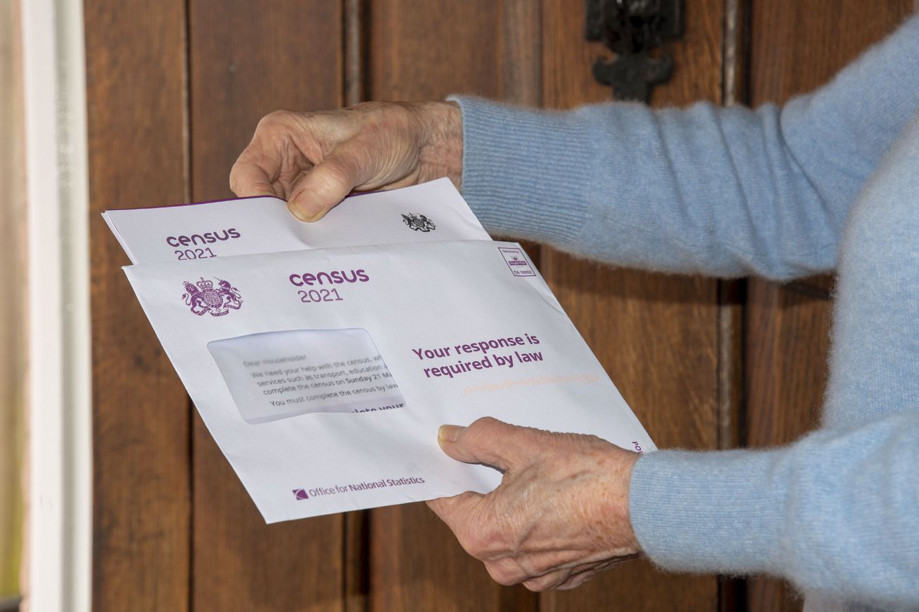 Mature woman at her front door opens documentaion relating to the UK Census, which every resident of England and Wales must complete.
