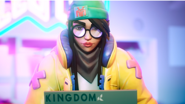 Valorant - A picture of the agent Killjoy, a young woman with dark hair, round glasses, a hat, and big jacket, on her laptop.
