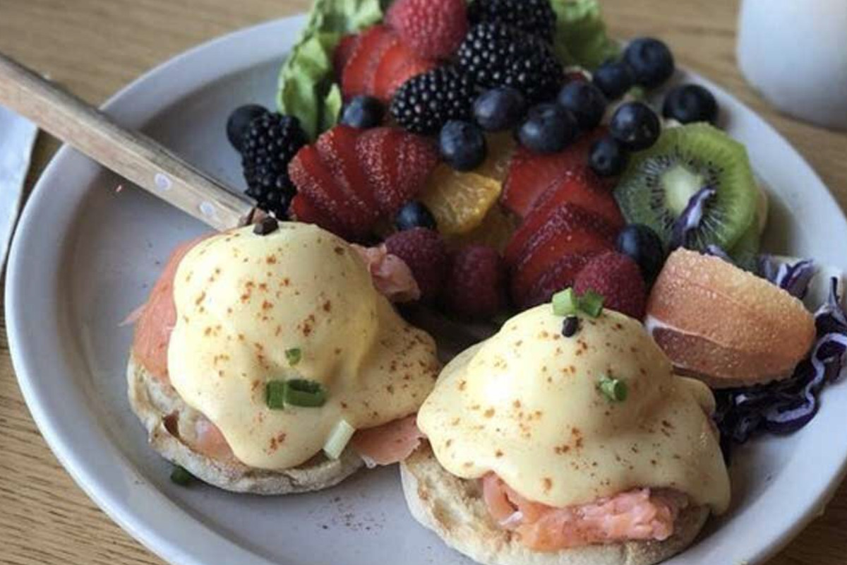 A Salmon Benedict with a side of assorted fruit on a white plate.