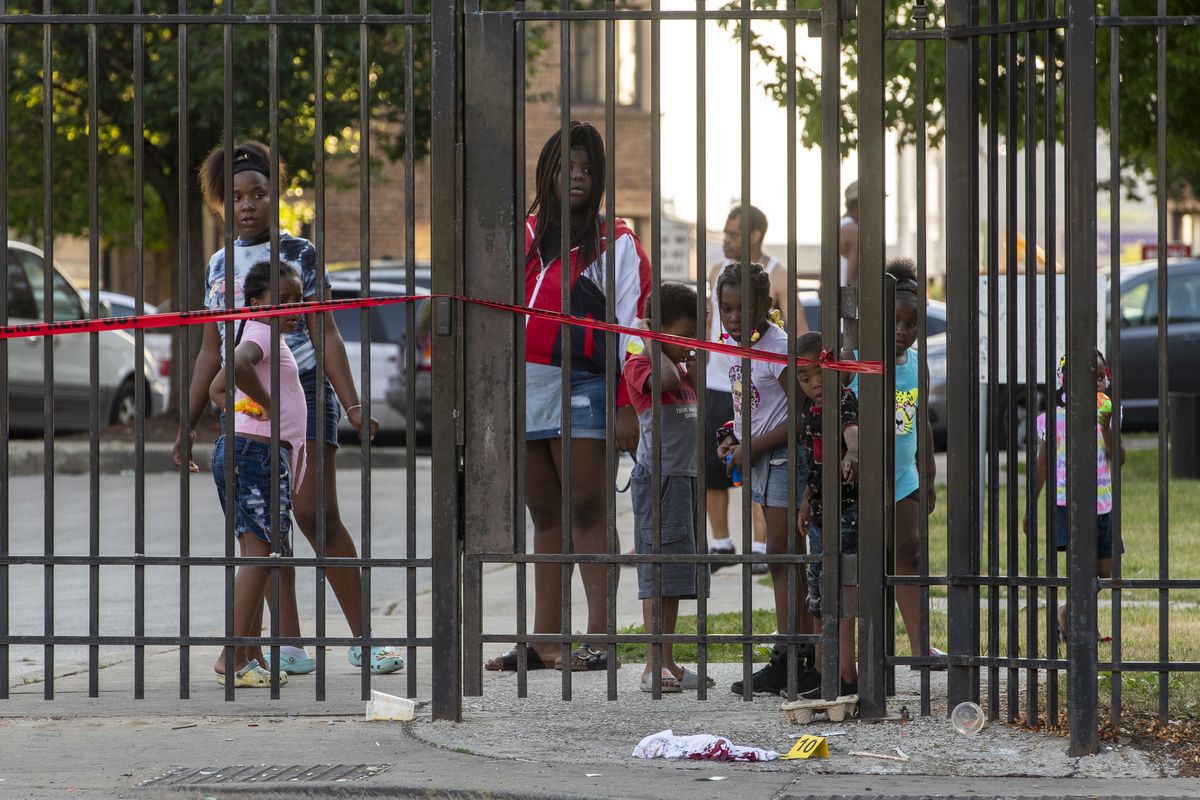 A group of children and other onlookers watch as Chicago police investigate in the 6400 block of South King Drive, where 31-year-old King Collier was killed in a drive-by shooting in Parkway Gardens, Friday evening, June 18, 2021.