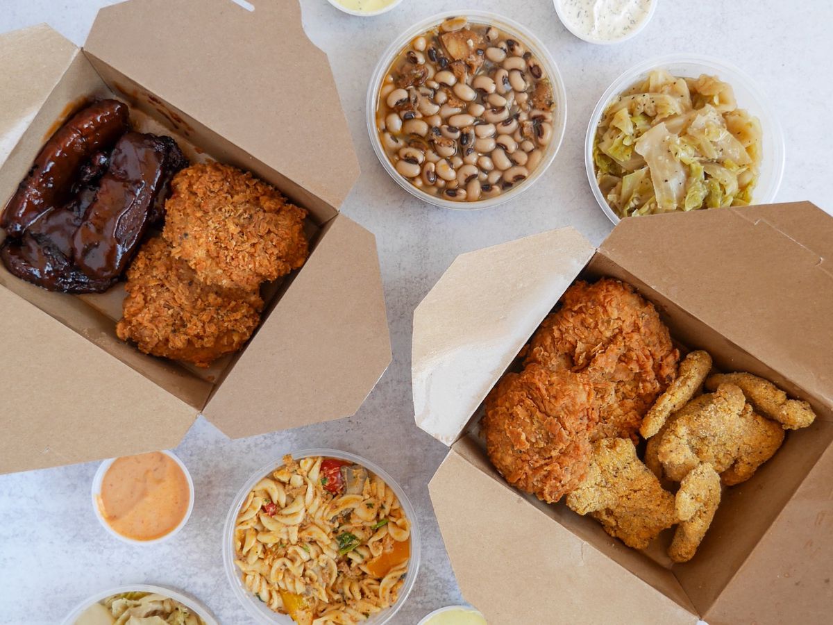 Two takeout boxes of fried and barbecue vegan meats from Dirty Lettuce, with sides of black-eyed peas, greens, and jambalaya
