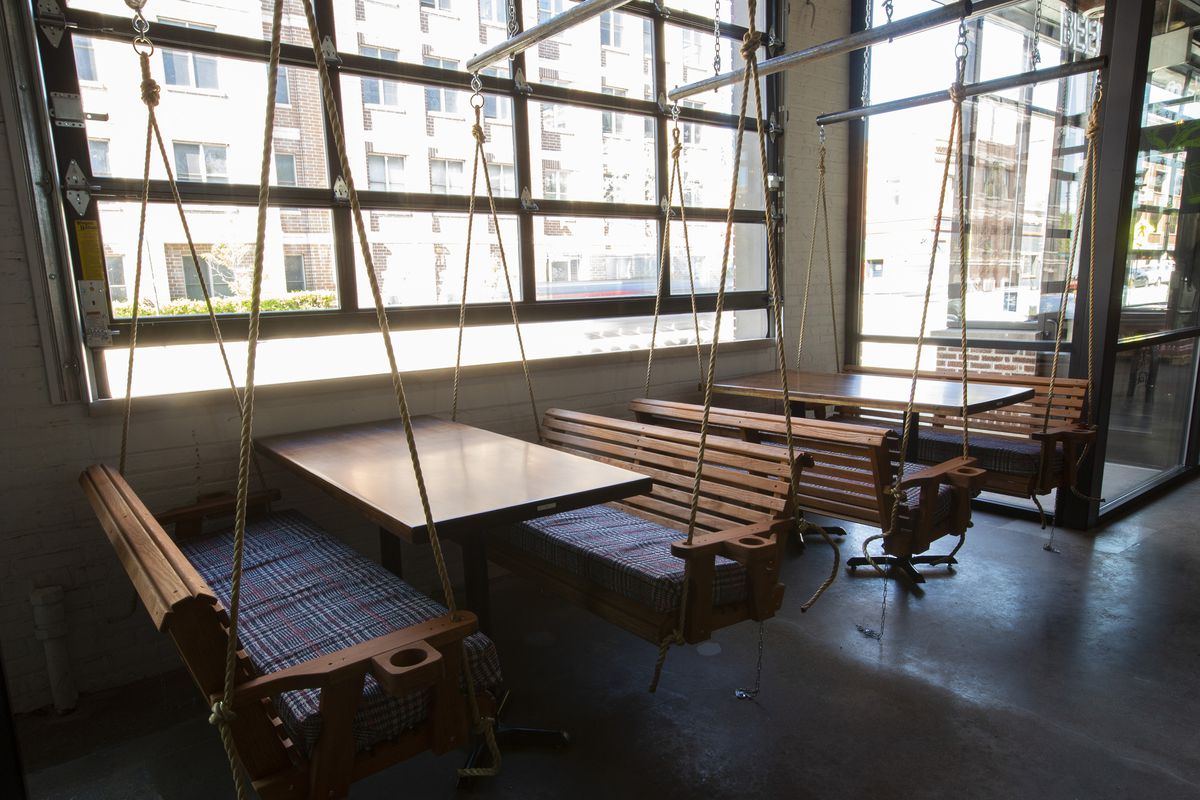 Wooden benches suspended by rope with tables by windows.