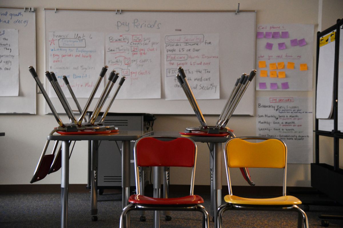 Chairs upside down on a table and two empty chairs sit in an empty classroom.