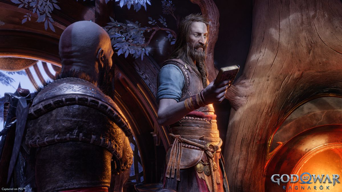 Tyr, standing next to a fireplace in Brok and Sindri’s home, looks at a book while Kratos watches in a screenshot from God of War Ragnarok