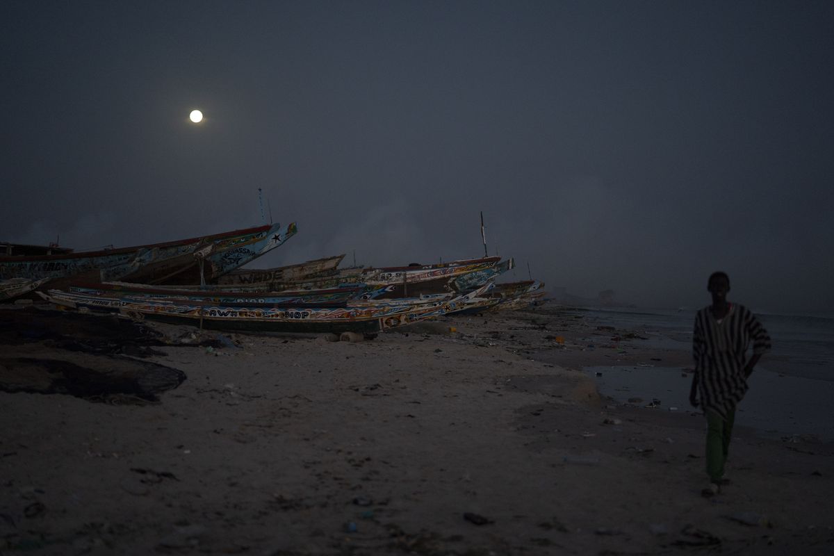 A man walks past pirogues used as fishing boats as the full moon rises over Bargny, Senegal.