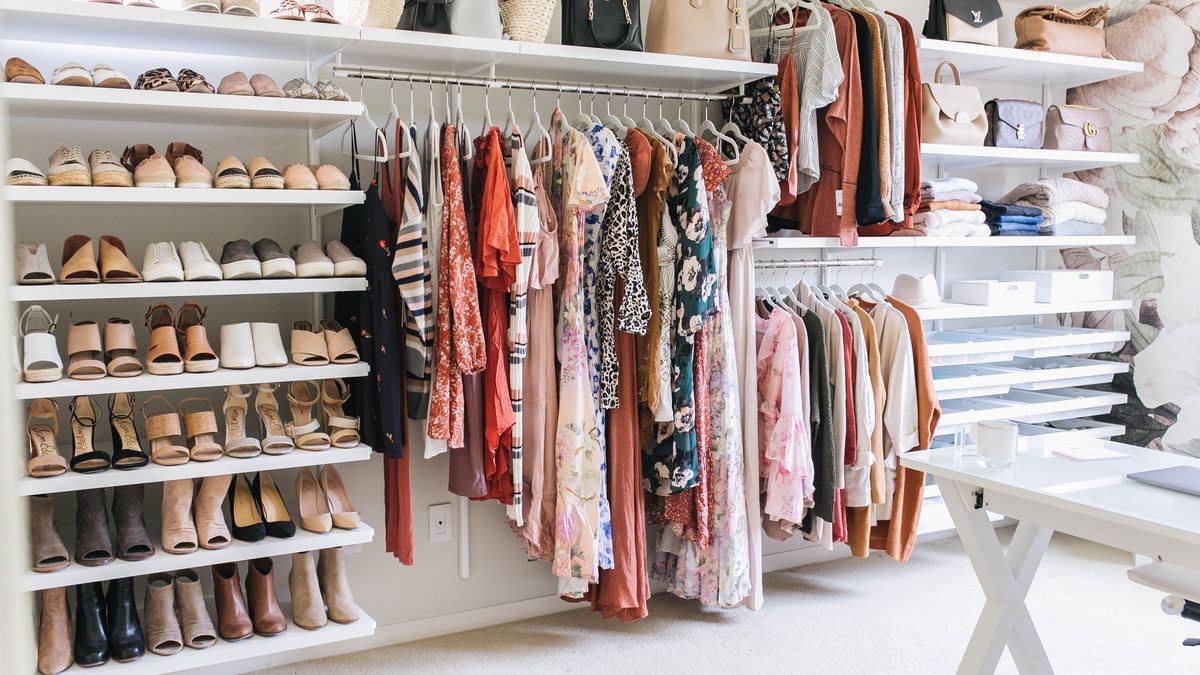 A custom closet features white shelves of shoes and hanging clothes from the Container Store. 