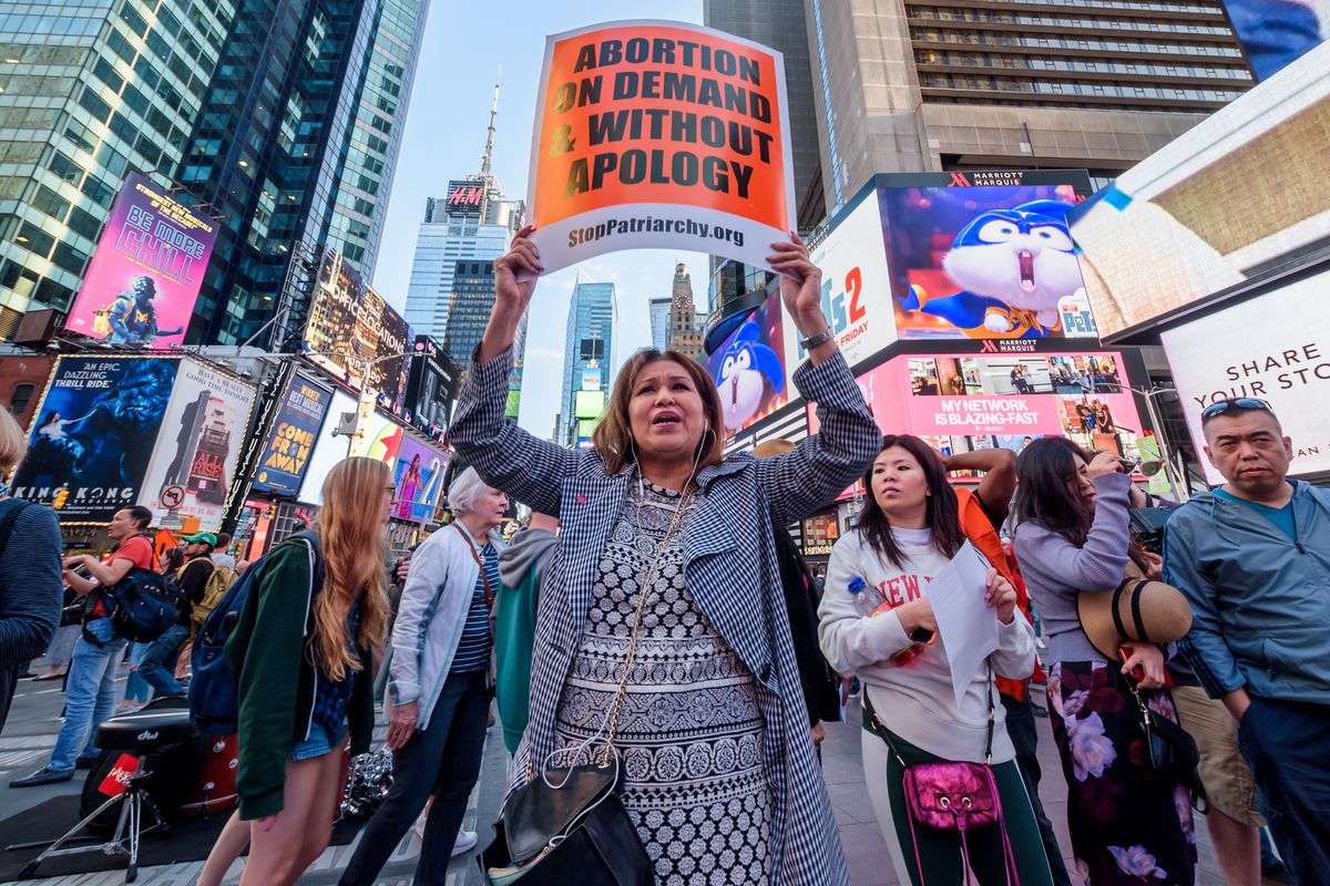 A protester holding a sign reading “Abortion on demand &amp; without apology” surrounded by other people in New York’s Times Square.
