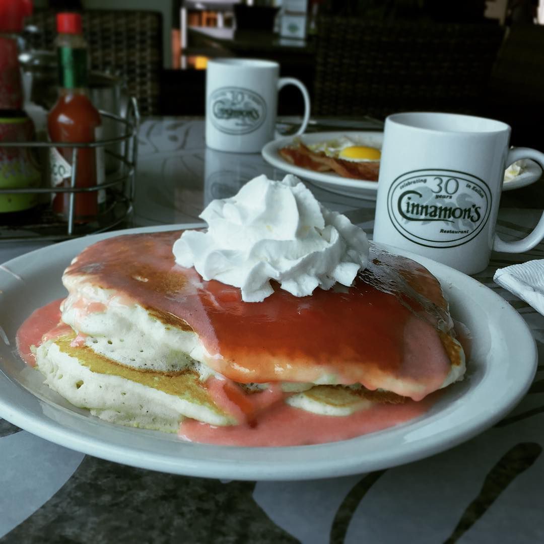 Two pancakes on a white plate with whipped cream and a pink sauce.